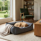 Textured plush dog bed in dark gray with black trim and tucked-in golden dog asleep.